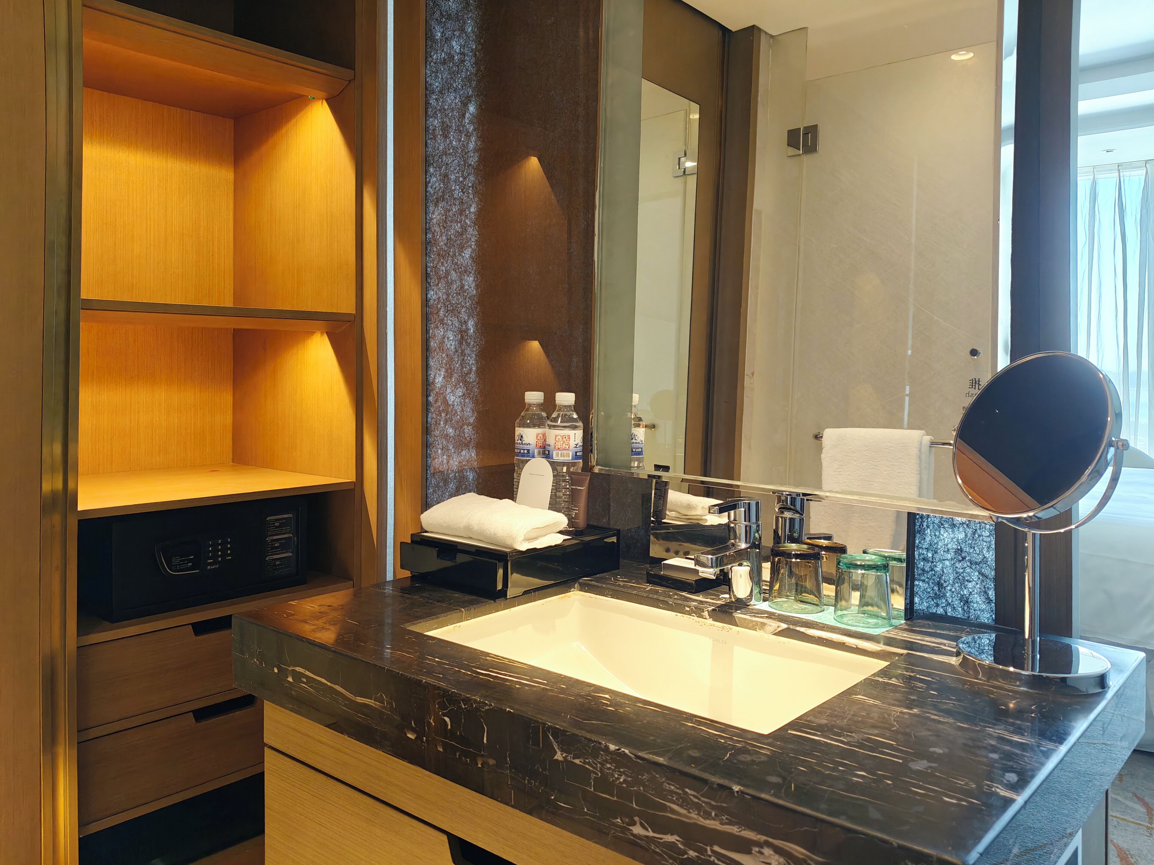 A modern bathroom with a marble sink, a large mirror, and a shelf with toiletries.