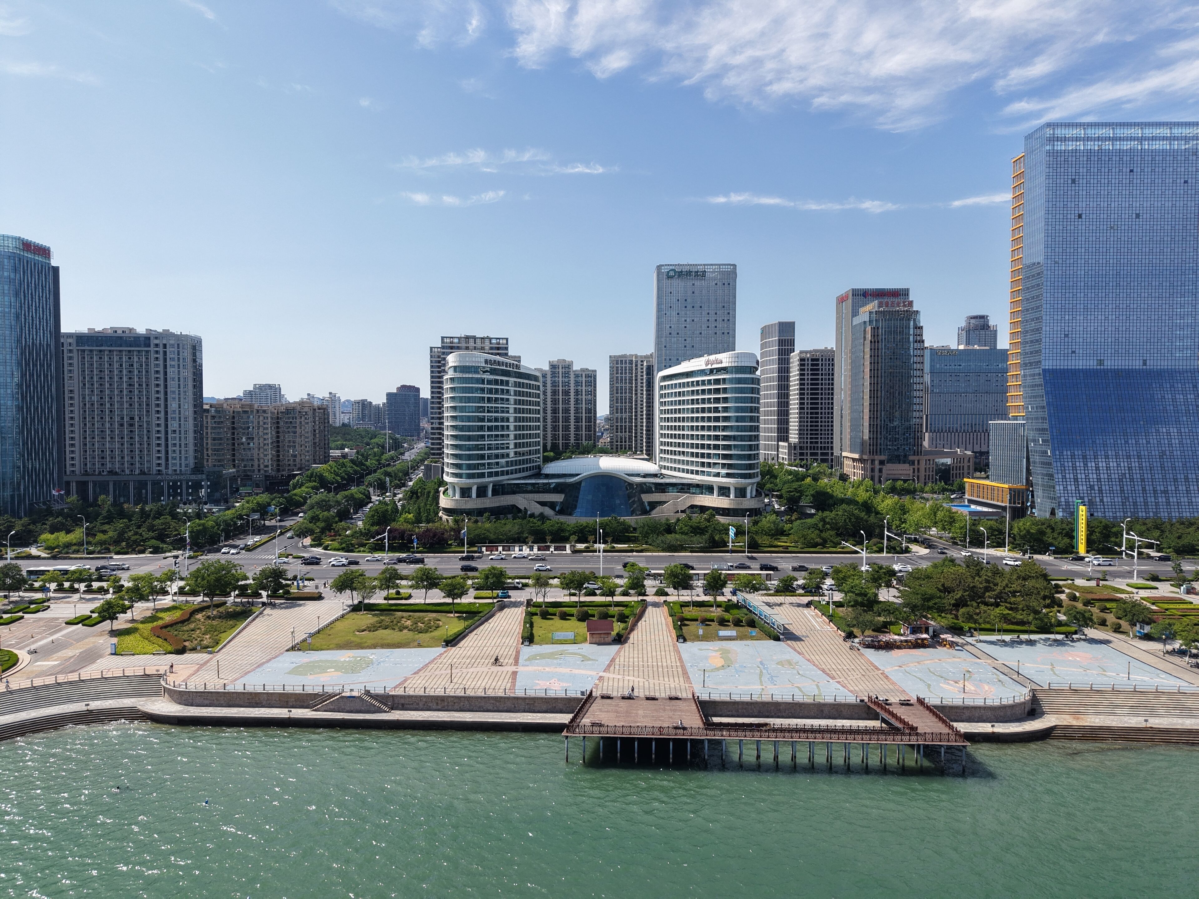 A modern cityscape with high-rise buildings, a waterfront promenade, and a distinctive curved building with a glass facade.