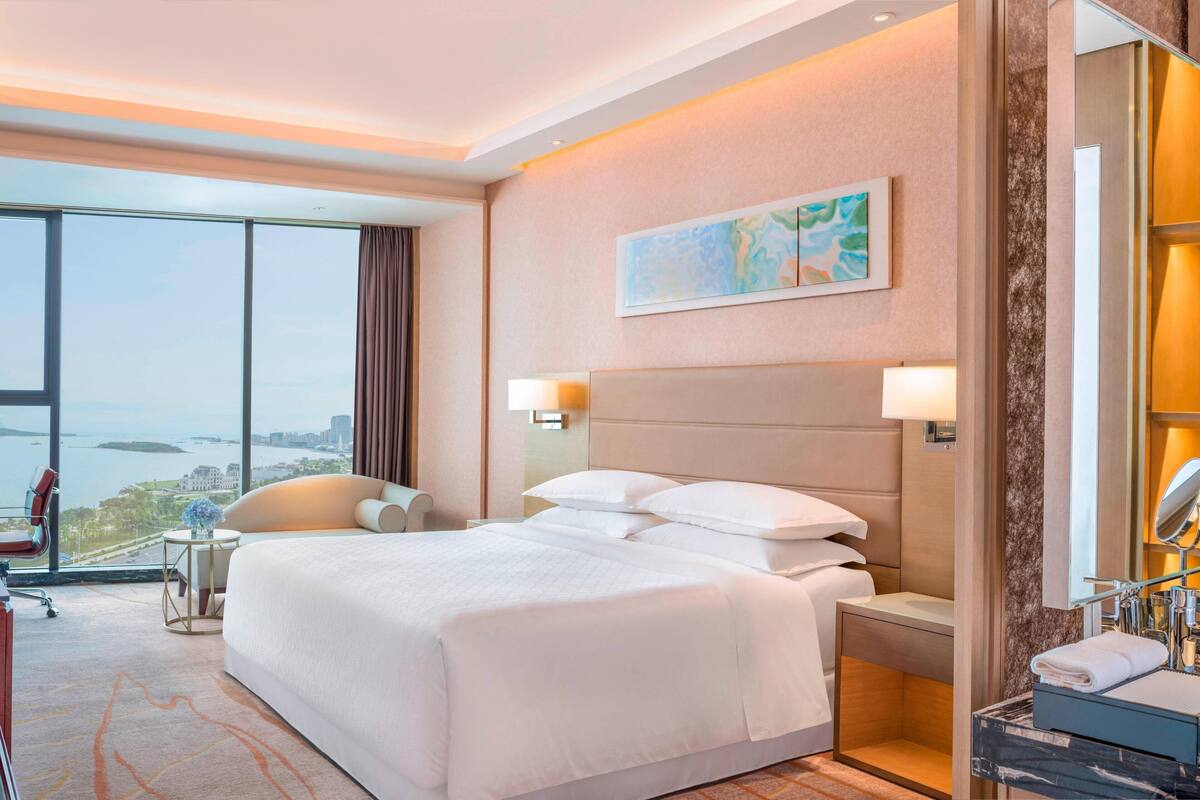 Hotelkamer met een groot bed, een bureau, een stoel, een badkamer met een spiegel en uitzicht op de stad door grote ramen.