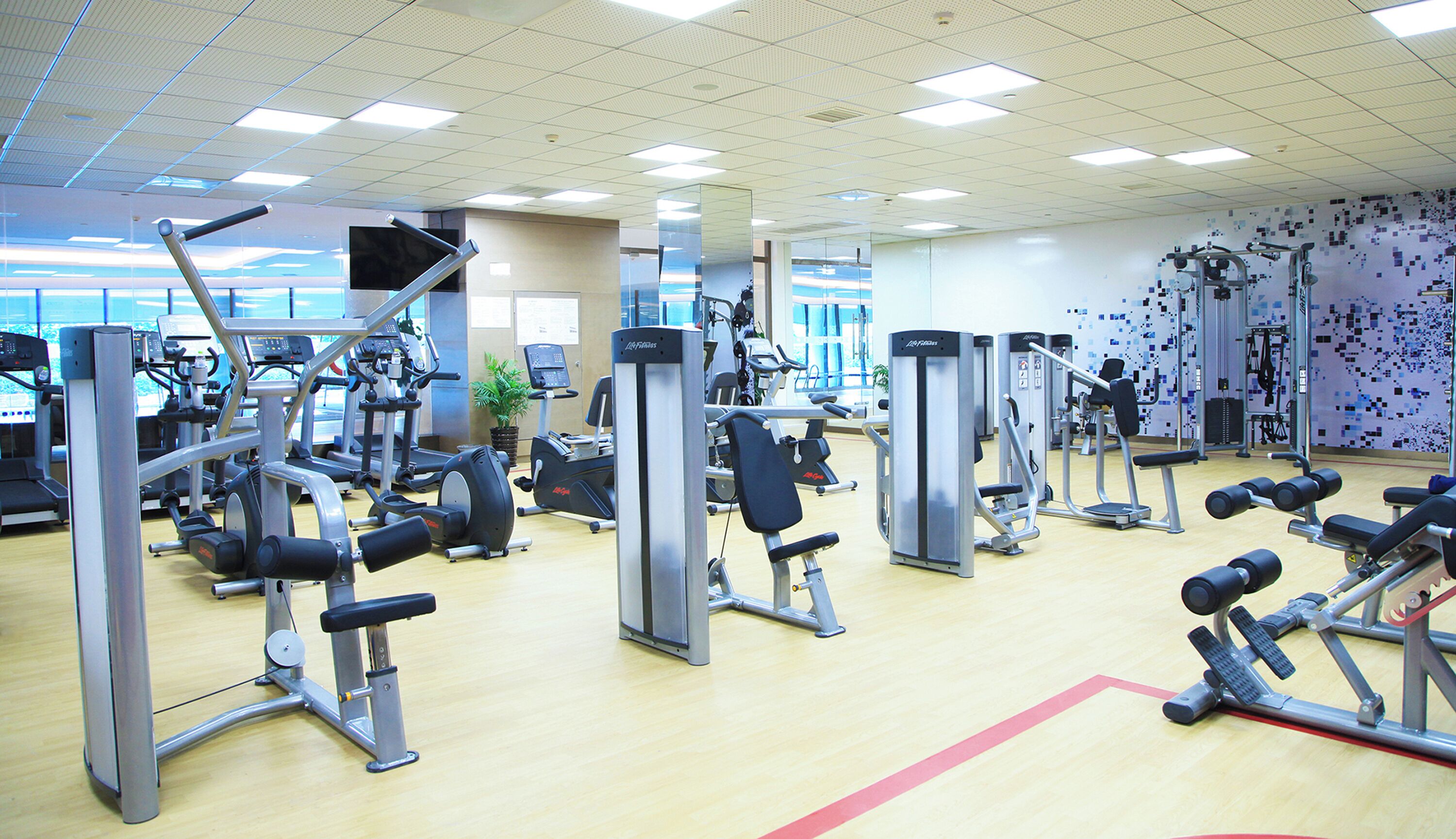A gym with various exercise machines, a large mirror, and a wall with a pixelated design.