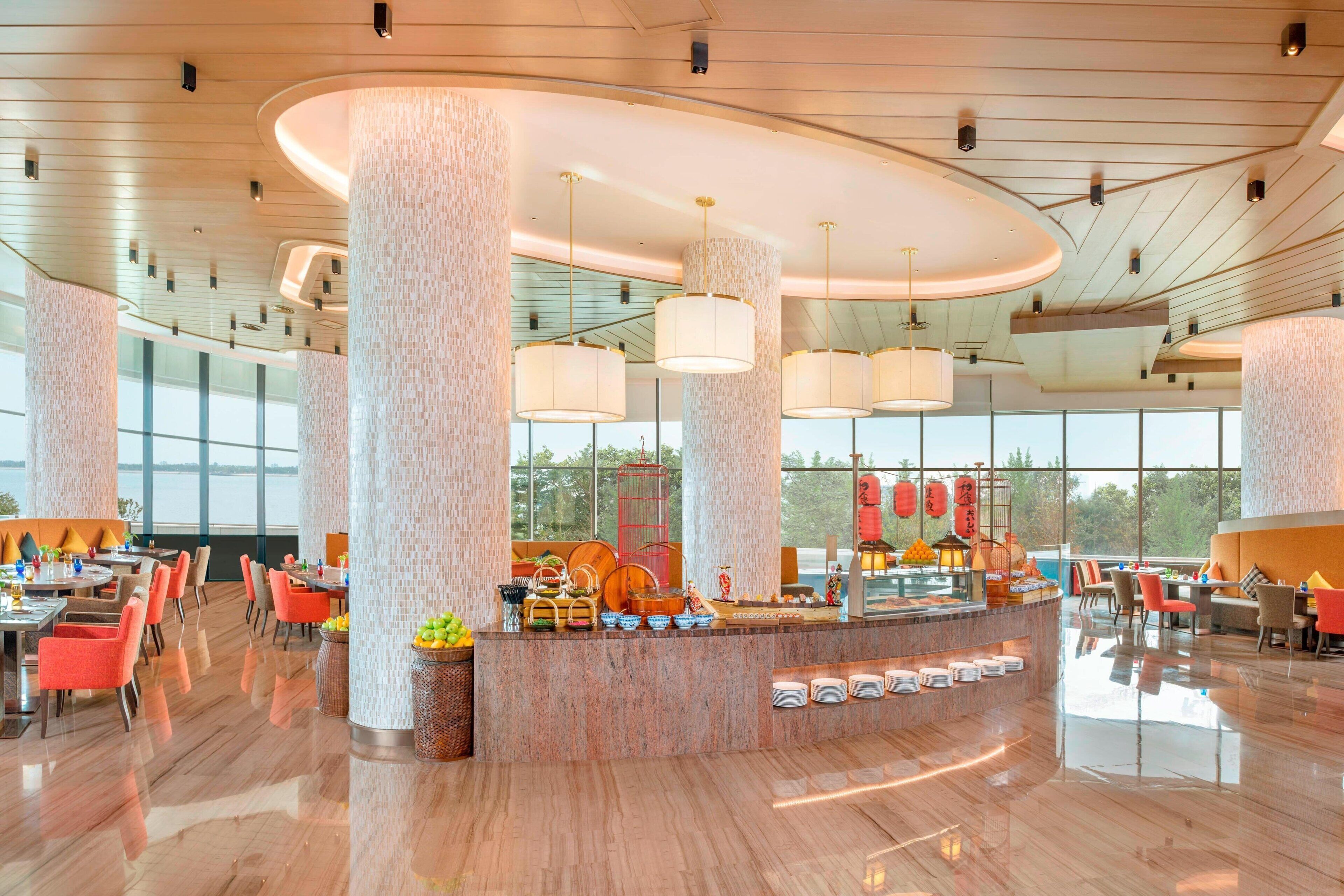 Een ruime hotellobby met hoge plafonds, grote zuilen en een centraal gelegen buffet.