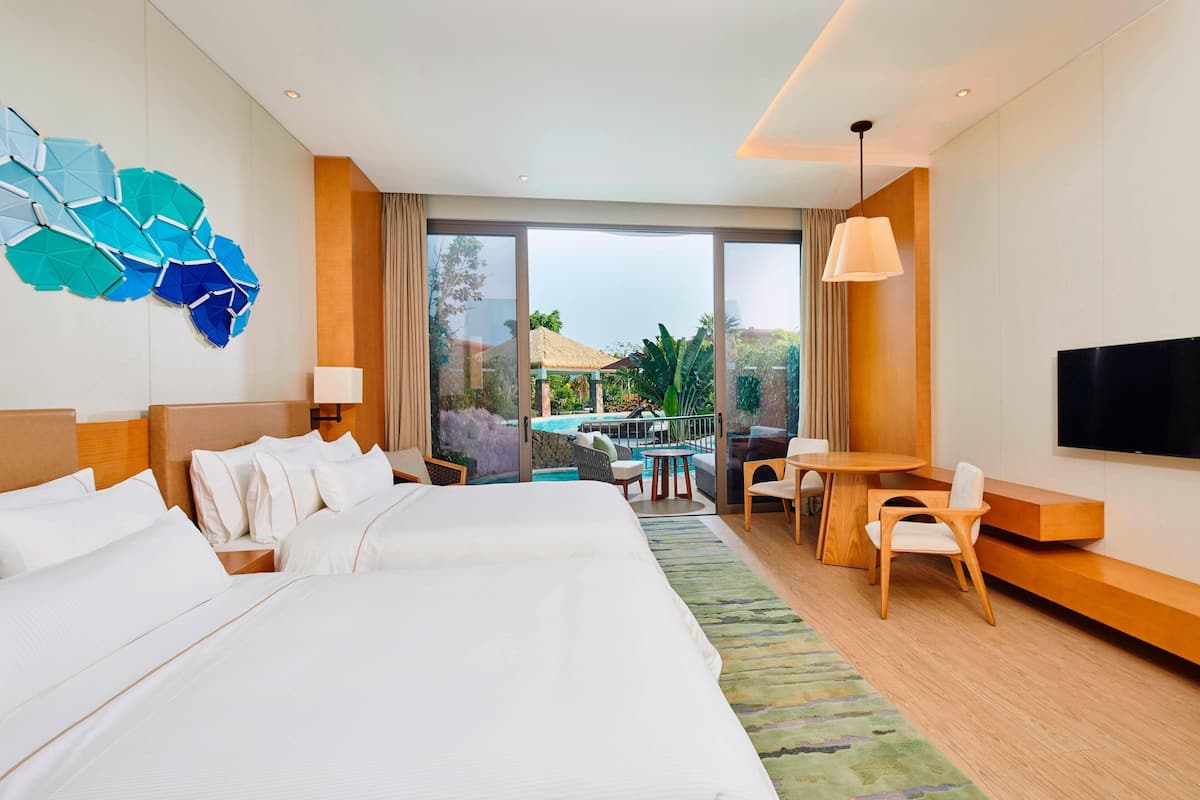 A hotel room with a large bed, a TV, a balcony with a pool view, and a dining area.