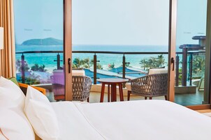 A hotel room with a large window offering a view of the ocean and a pool area.