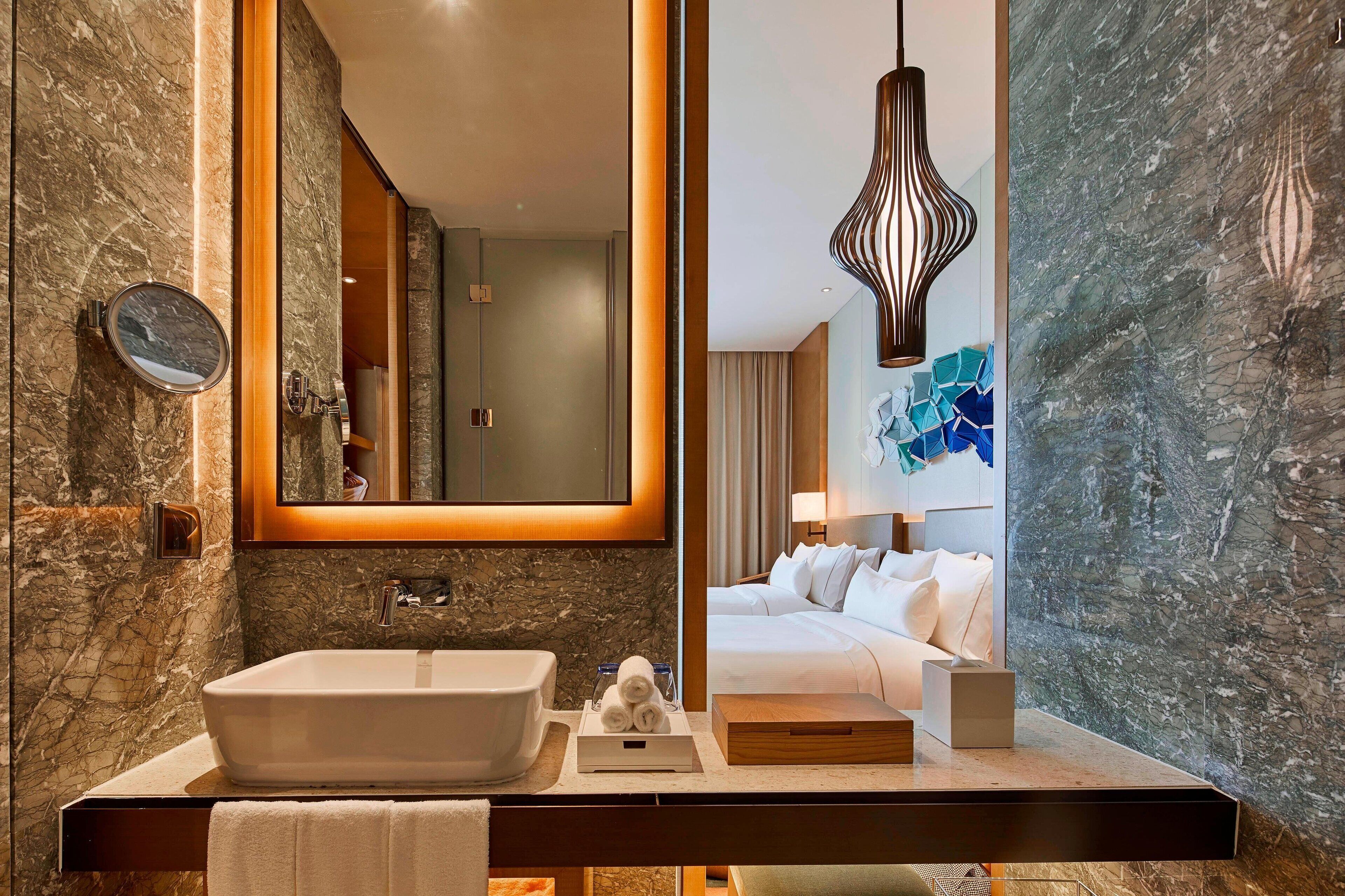 Une salle de bain moderne avec un lavabo en marbre, un grand miroir et un luminaire suspendu au design contemporain.