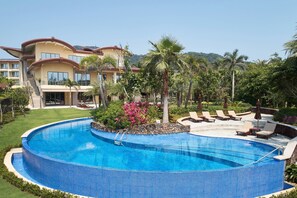 Relax by the resort's large, curved pool surrounded by lush greenery and comfortable lounge chairs.