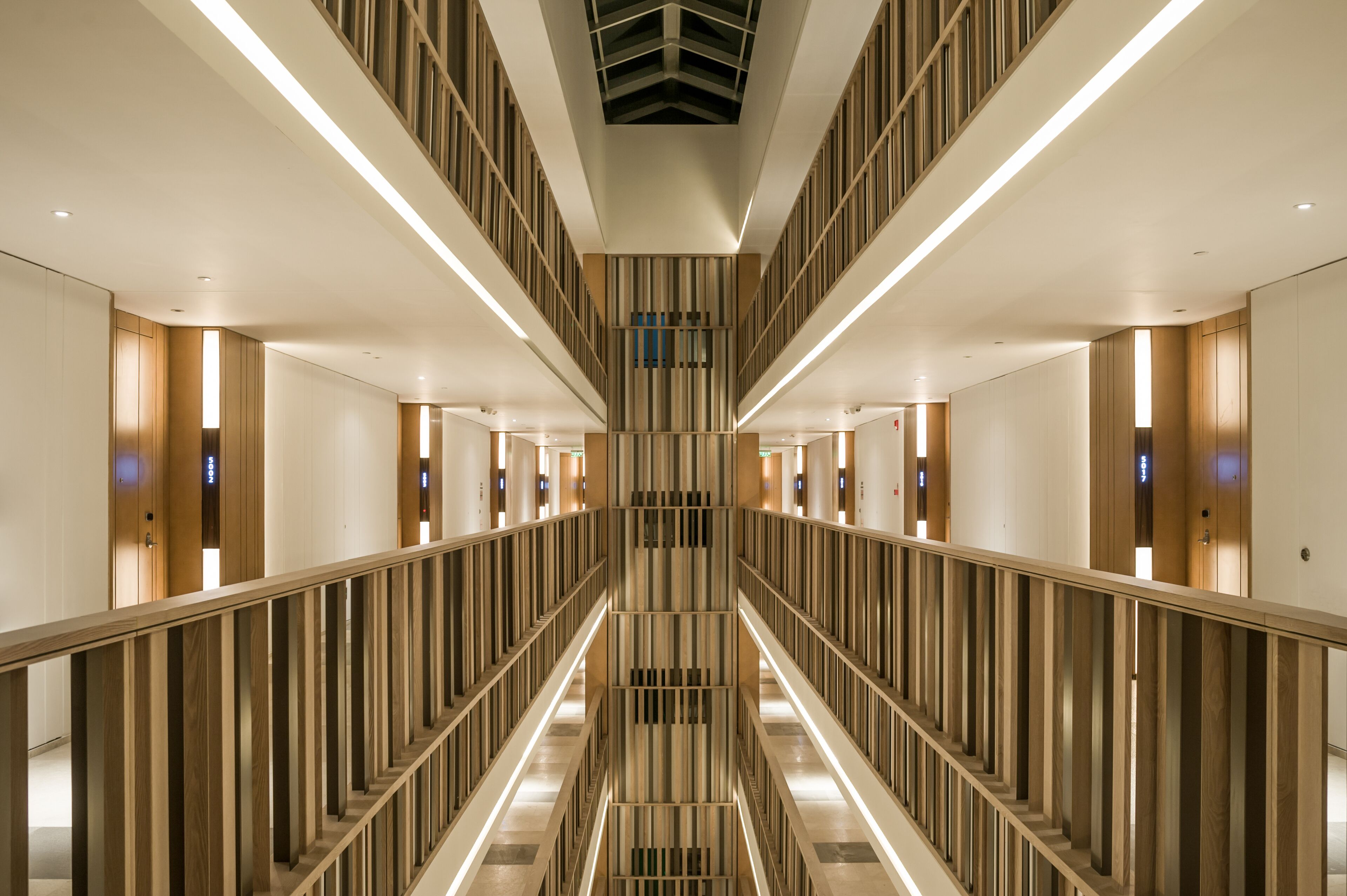A modern hotel corridor with a central staircase, wooden paneling, and illuminated handrails.