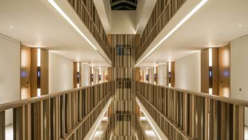 A modern hotel corridor with a central staircase, wooden paneling, and illuminated handrails.