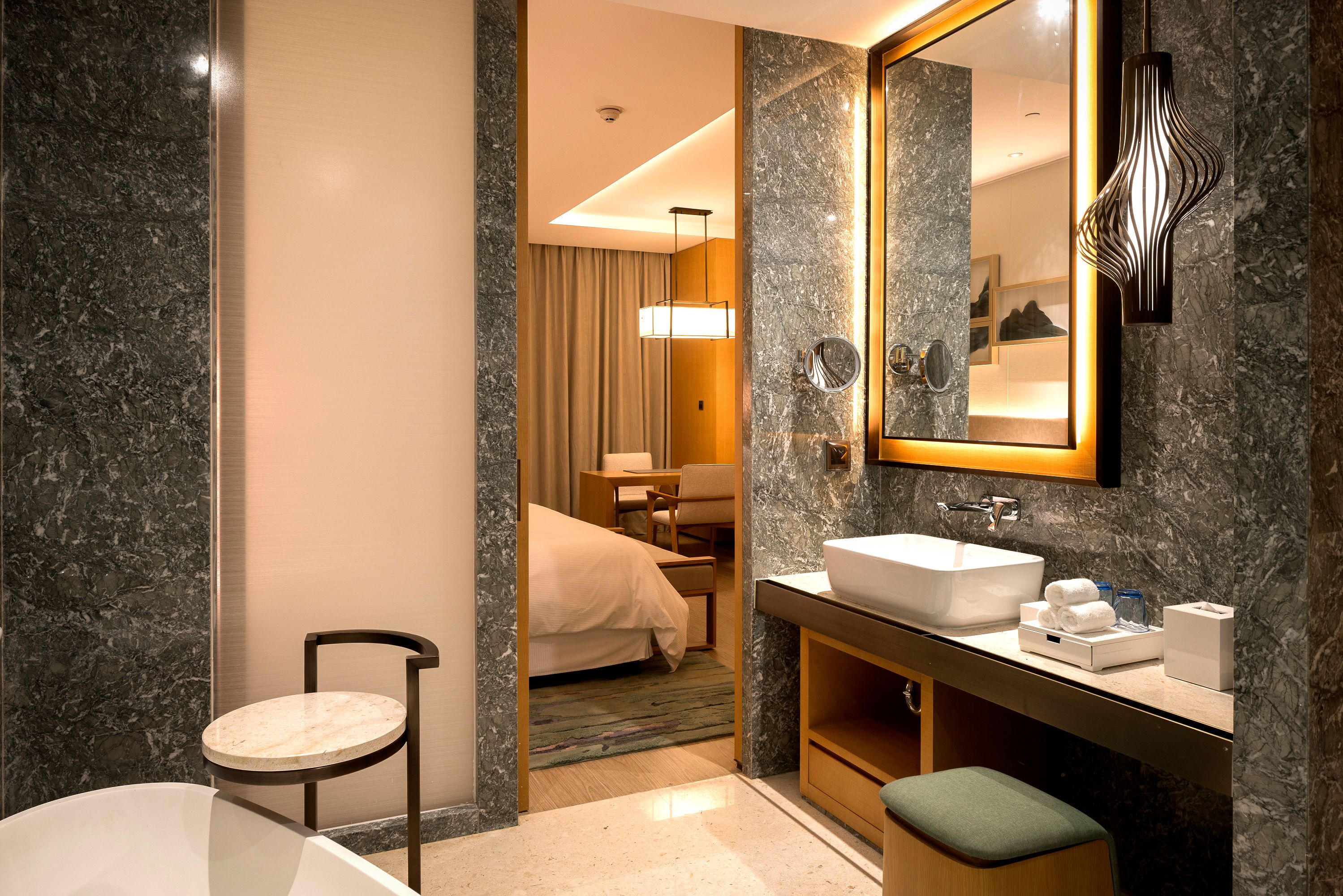 A modern bathroom with a marble sink, a bathtub, and a mirror.