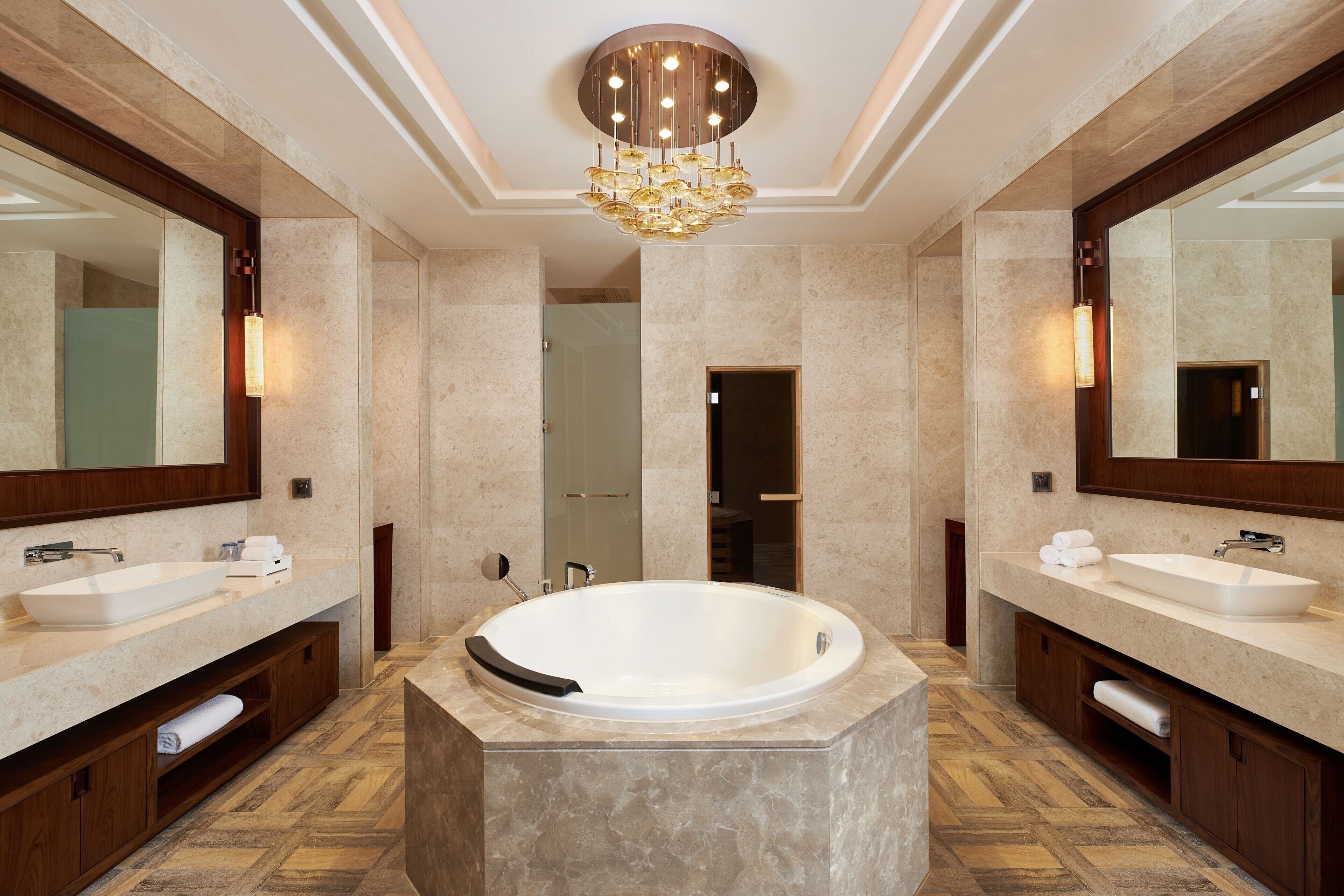 A modern bathroom with two sinks, a large bathtub, and a chandelier.