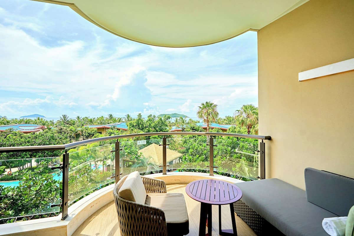 A balcony with wicker furniture, a small round table, and a view of a pool and greenery.