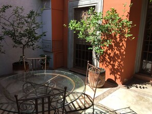 A glass-top table with metal chairs, a potted plant, and a door with a metal gate.