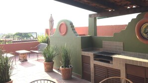 Une terrasse extérieure avec un barbecue, des plantes en pot et une vue sur la ville.