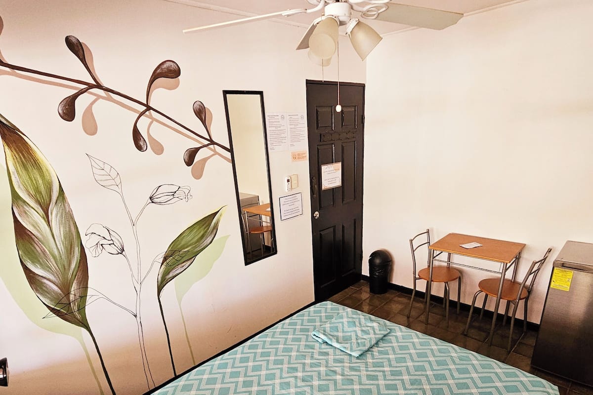 Une pièce comprenant un lit, un bureau, une chaise, un ventilateur de plafond et une porte.