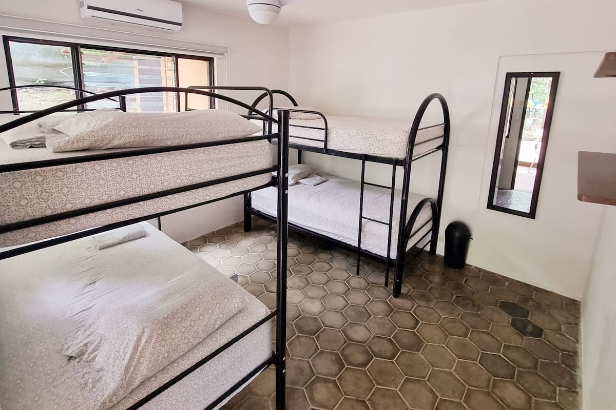 Une chambre de dortoir avec des lits superposés, un ventilateur de plafond, un appareil de climatisation et un sol carrelé.