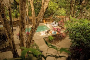 A pool area with lounge chairs and a table, surrounded by trees and plants. - Casa Pura Vida Surf Hostel (Tamarindo)
