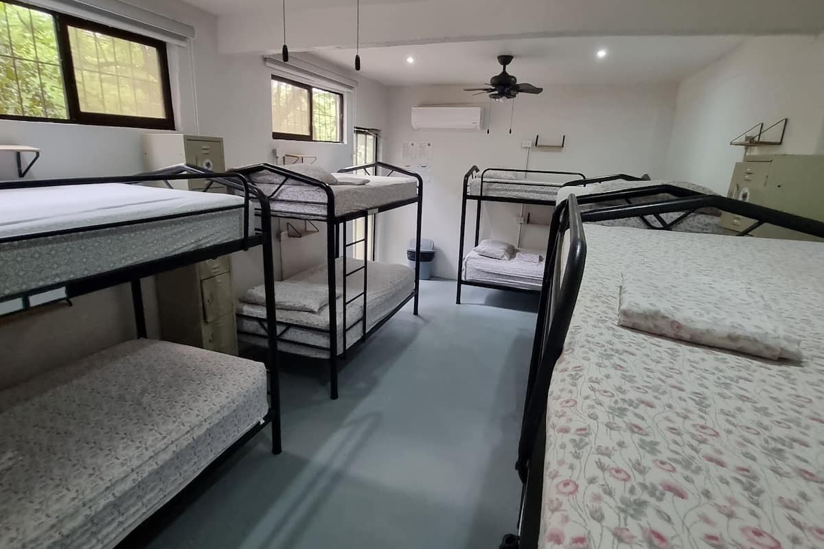 Une chambre de dortoir avec des lits superposés, un ventilateur de plafond et une fenêtre.