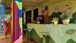 Un área de recepción colorida con una pared verde y amarilla, un mostrador de recepción y una hamaca.