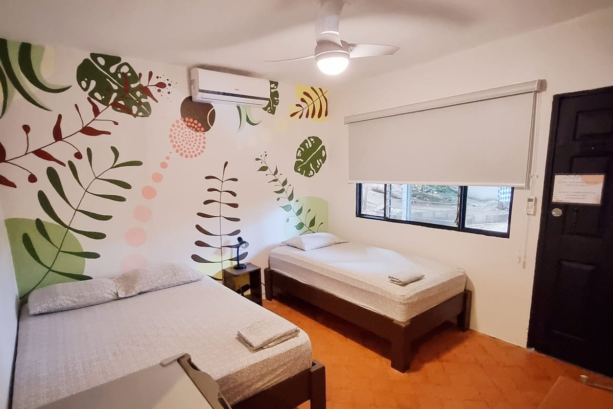 Une chambre de taille modeste, équipée de deux lits, d’un ventilateur de plafond et d’une fenêtre donnant sur un paysage agréable.