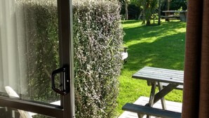 A view from inside a room with a glass door leading to an outdoor patio area. - Piha Beachstay - Hostel (Piha)
