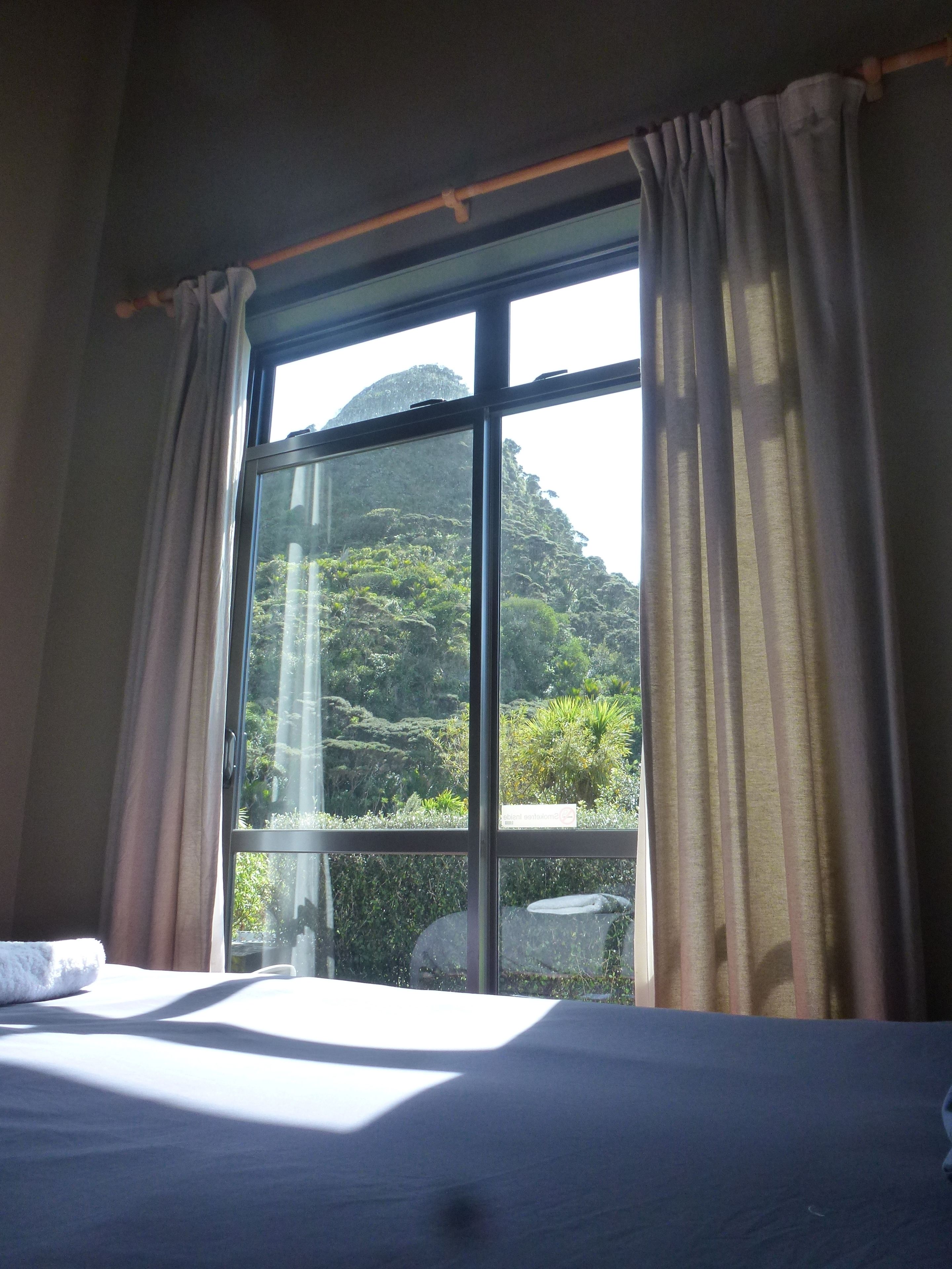 A room with a large window, a bed, and a view of a mountainous landscape.