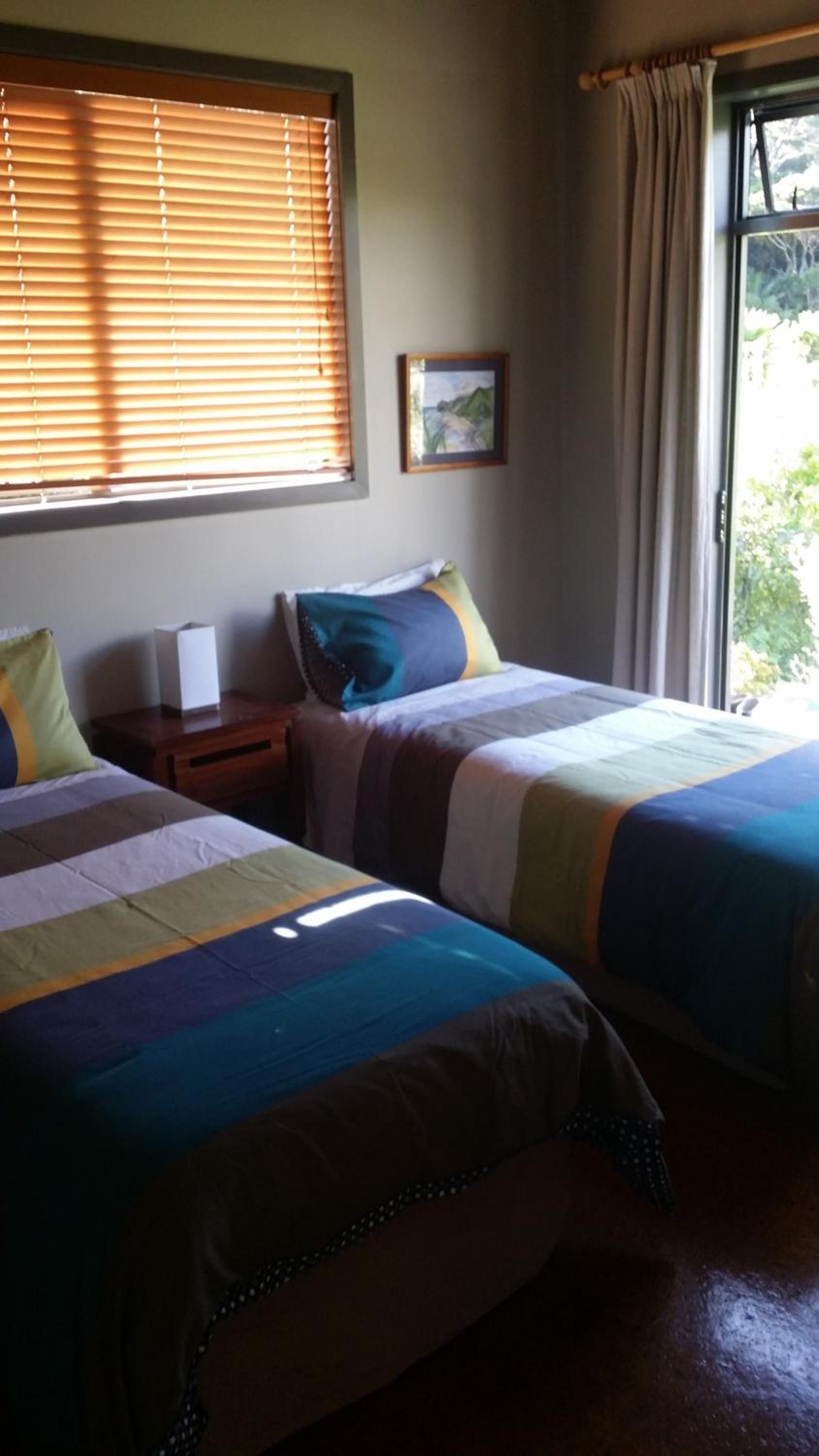A room with two beds, a nightstand, a framed picture, and a window with curtains.