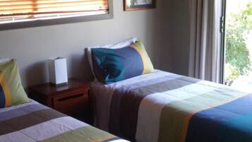 A room with two beds, a nightstand, a framed picture, and a window with curtains.