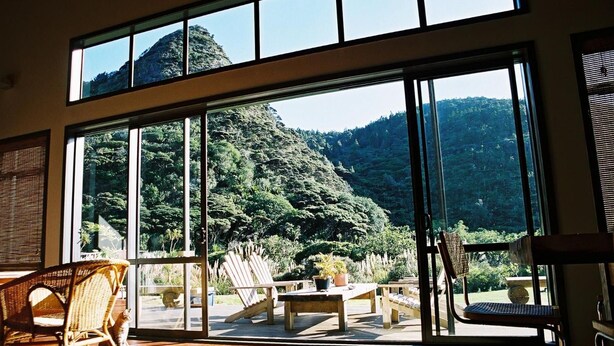 A spacious room with large windows offering a view of a lush forested mountain. - Piha Beachstay - Hostel (Piha)