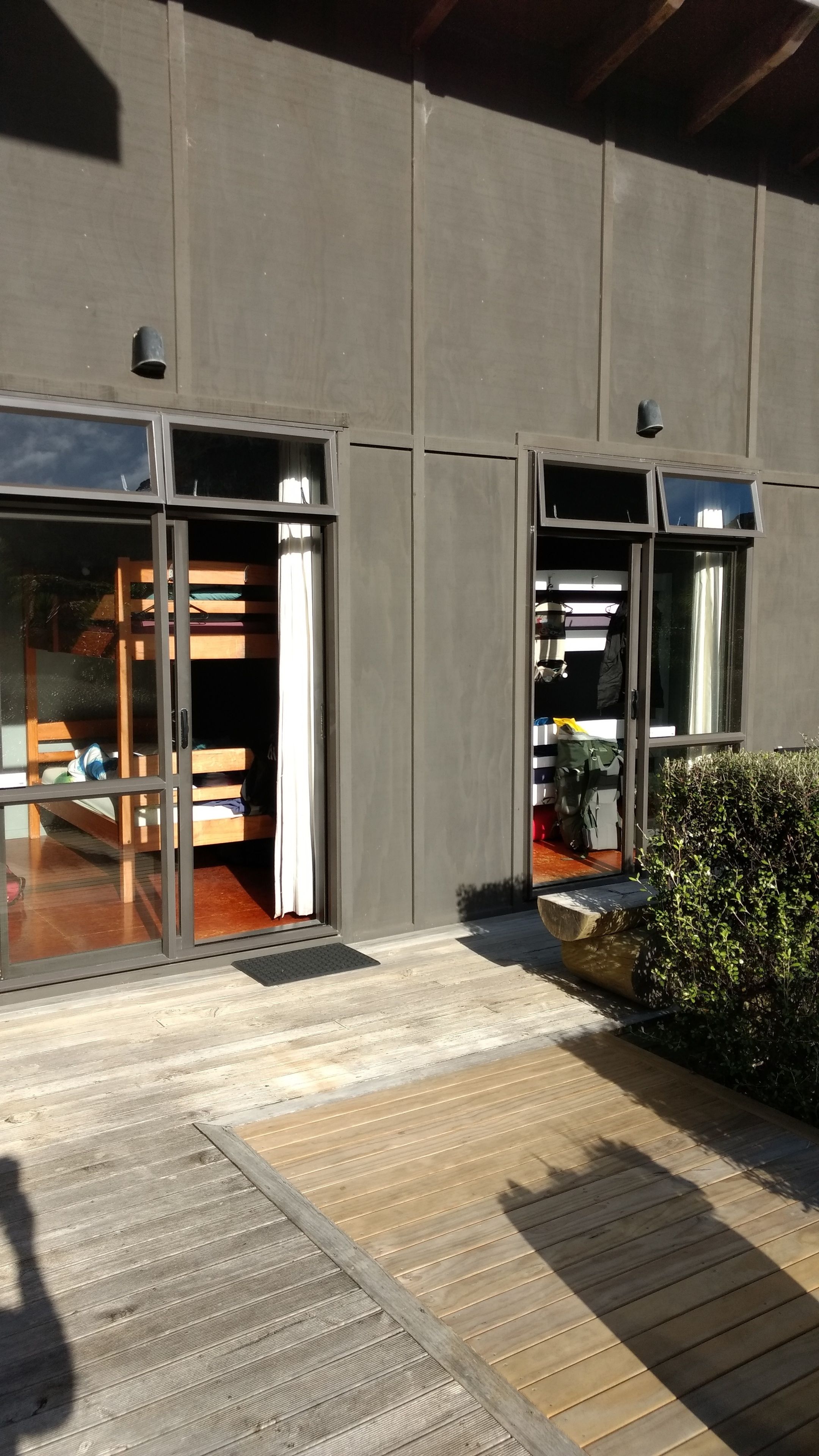 Un bâtiment moderne doté de grandes portes vitrées qui donnent sur une pièce avec des lits superposés et une terrasse en bois.
