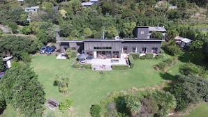 A modern two-story house with a large front yard, surrounded by dense forest. - Piha Beachstay - Hostel (Piha)