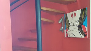 A spiral staircase with wooden steps and a blue central pole, leading to a red-walled room with a colorful artwork on the wall. - Duplex Apartment in Miraflores (Lima)