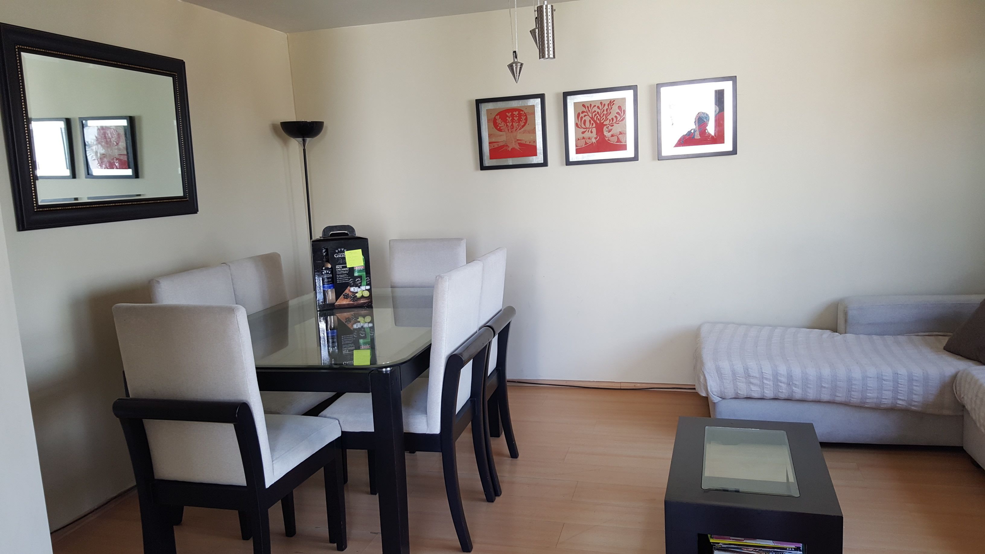 A dining area with a glass table, four chairs, a coffee machine, and framed artwork on the wall.