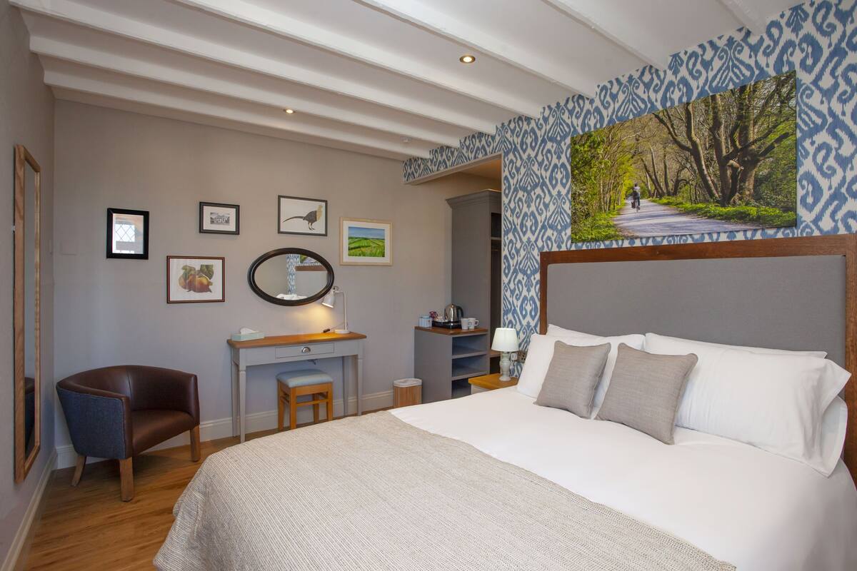 Een slaapkamer met een groot bed, een bureau met stoel, een spiegel en fotolijstjes aan de muur.