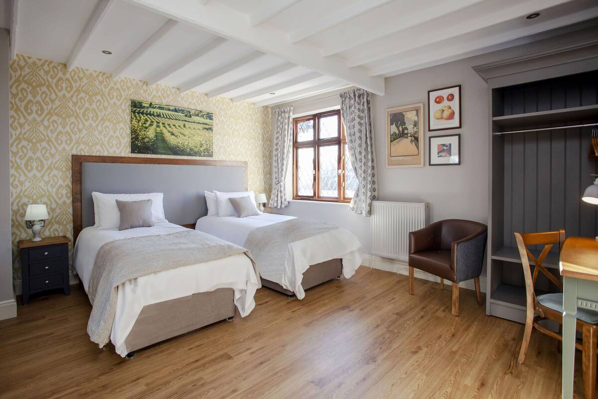 Een slaapkamer met twee bedden, een houten vloer, een raam met gordijnen, een radiator en een stoel.