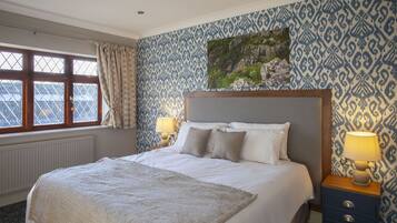 A hotel room with a large bed, two bedside lamps, a patterned wallpaper, and a window with curtains.
