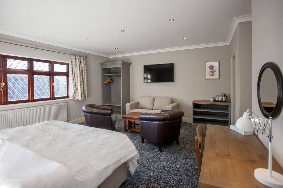Een hotelkamer met een bed, een slaapbank, een houten tafel, een televisie en een raam met gordijnen.