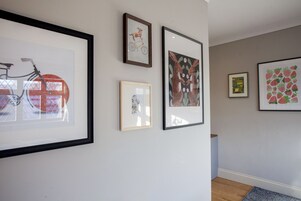 A hallway with framed artwork on the walls, including a bicycle, a dog, and a strawberry pattern.