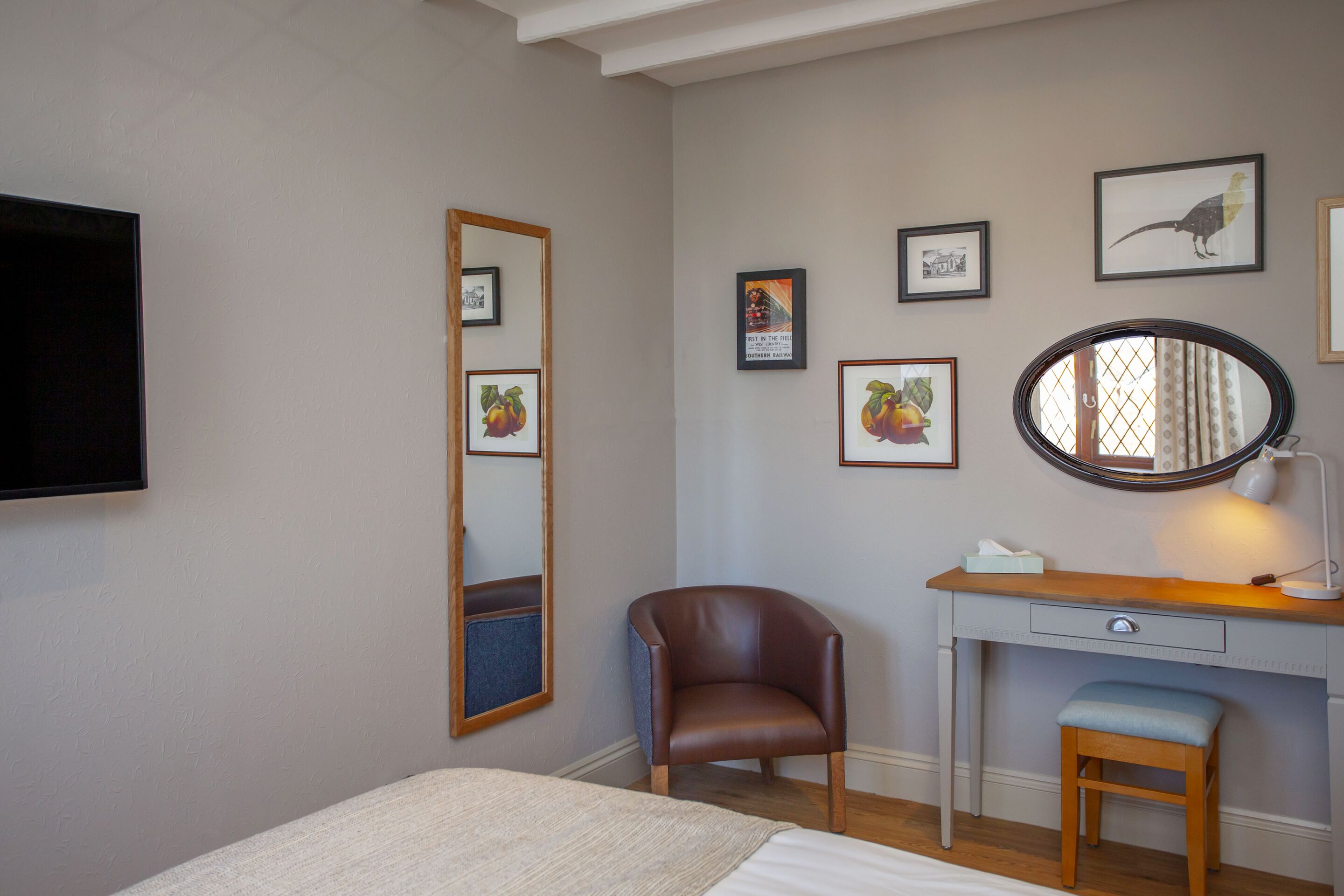 Une chambre à coucher avec un lit, un bureau avec une chaise, un miroir et des tableaux encadrés au mur.