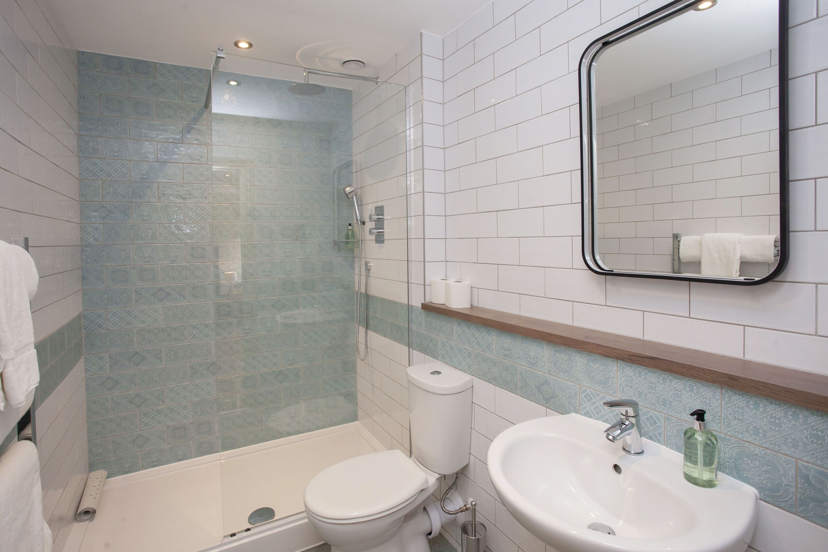 Een badkamer met douche, toilet, wastafel en spiegel.