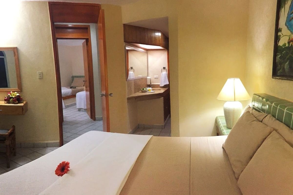 A hotel room with a bed, a desk with a lamp, a chair, and a bathroom visible through an open door.