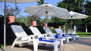 A row of white lounge chairs with blue towels, white umbrellas, and red planters in a garden setting. - Coral Ixtapa (Ixtapa)