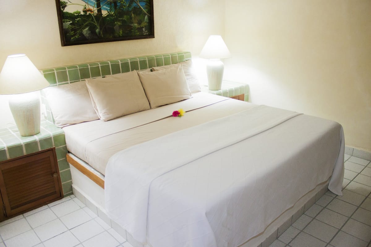 A neatly made bed with a green headboard, two bedside lamps, and a small flower on the bed.