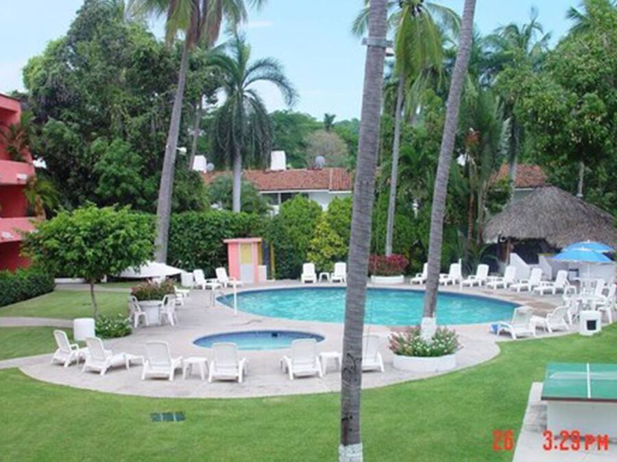 A pool area with lounge chairs, palm trees, and a thatched-roof structure.
