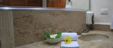 Un baño con lavamanos de mármol, una toalla y un cuenco con flores.