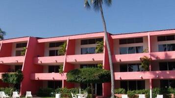 Un hotel de varios pisos con fachada roja, balcones y un área de piscina con sillones de descanso.