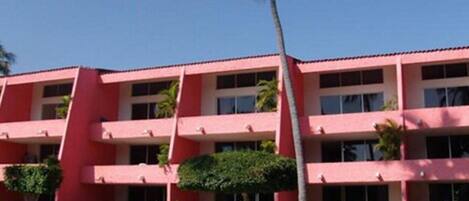 A multi-story hotel with a red facade, balconies, and a pool area with lounge chairs.