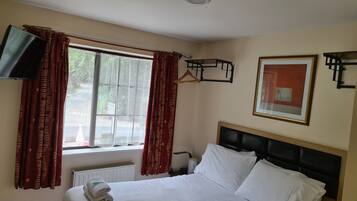 Une chambre d’hôtel avec un lit, un téléviseur fixé au mur, un radiateur et une fenêtre avec des rideaux.