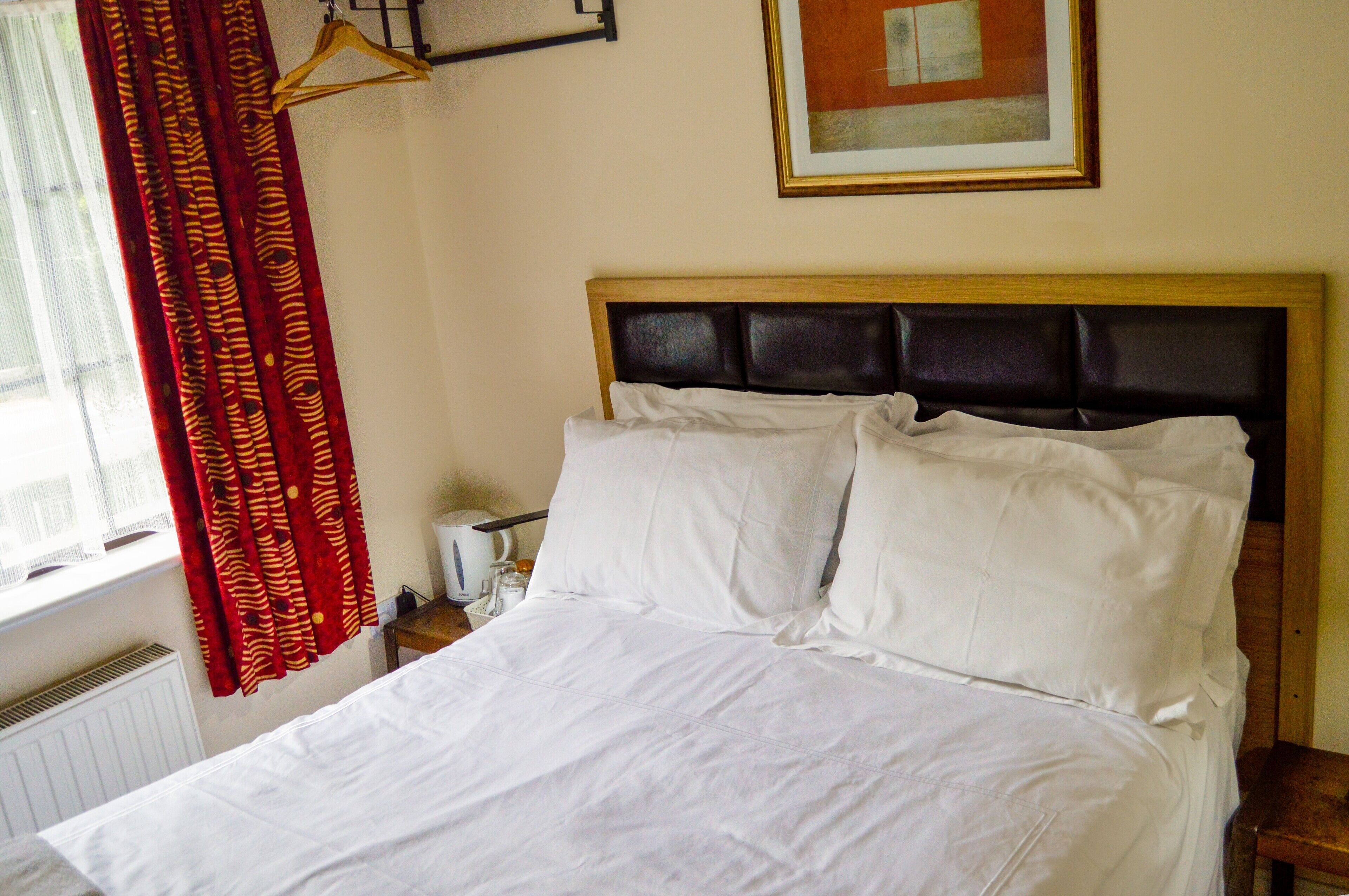 A neatly made bed with white linens, a wooden headboard, and a red patterned curtain.