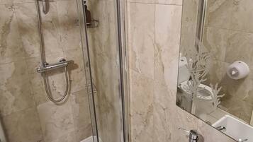 Un baño con ducha de vidrio, un lavamanos blanco con dispensador de jabón negro y un espejo sobre el lavamanos.