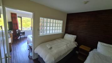 A bedroom with a single bed, a window with decorative glass, a wooden headboard, and a desk with a chair.