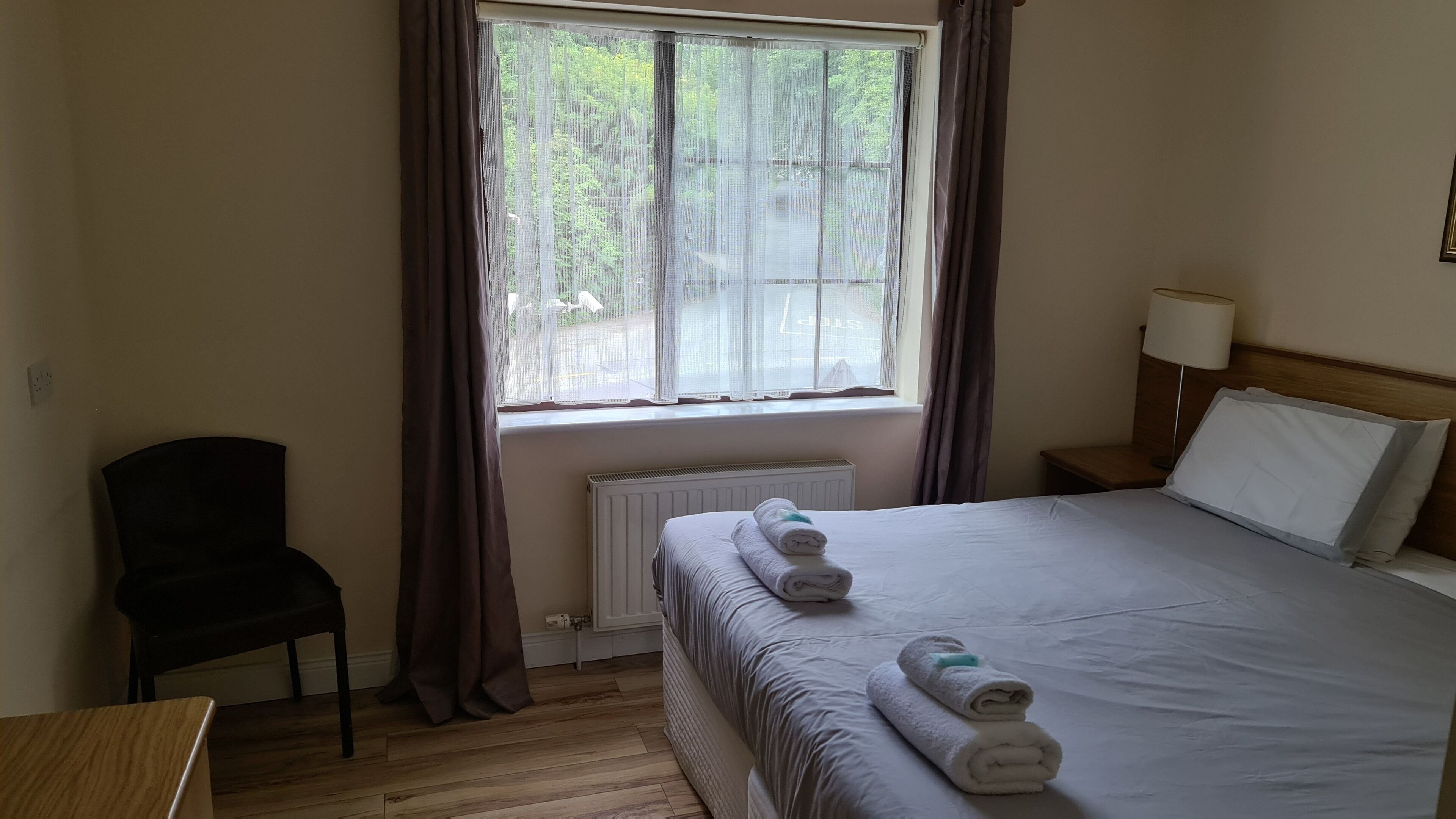 A hotel room with a bed, a chair, a nightstand, a lamp, and a window with curtains.